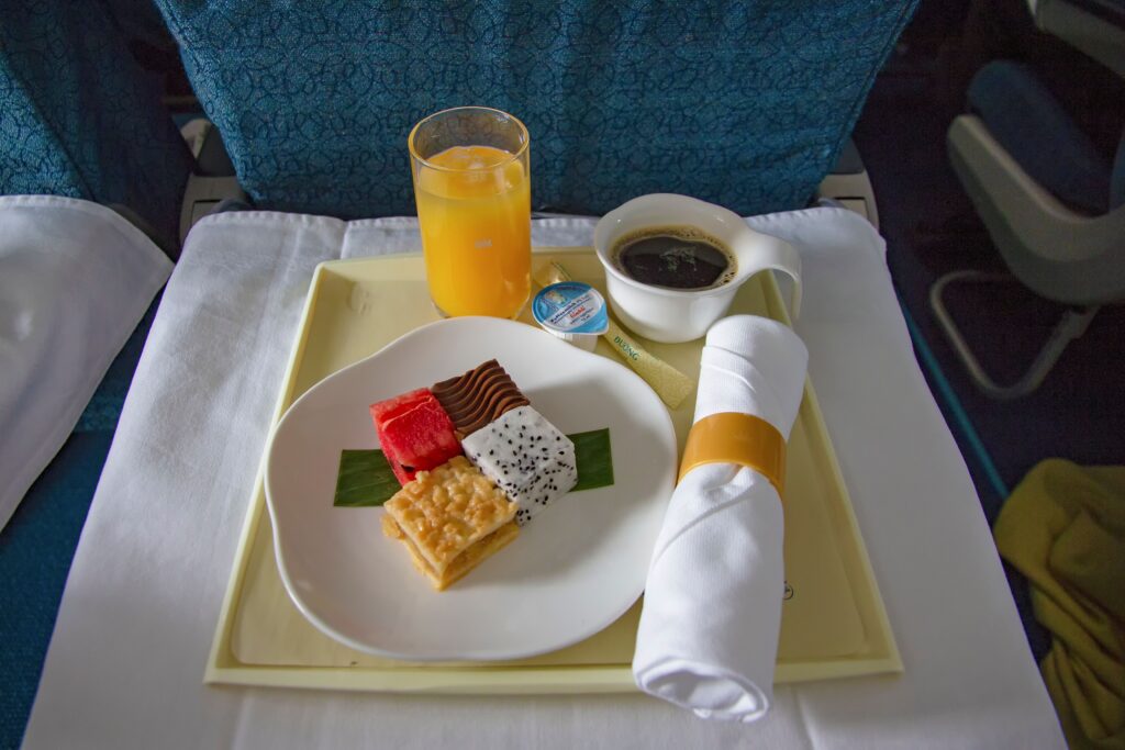 A colorful in-flight meal tray featuring desserts, orange juice, and coffee. Flight booking . Travoaid .